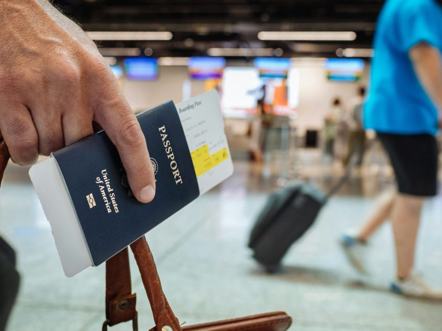 Osoba na fotografii drží v ruke medzi prstami pas občana Spojených štátov amerických.