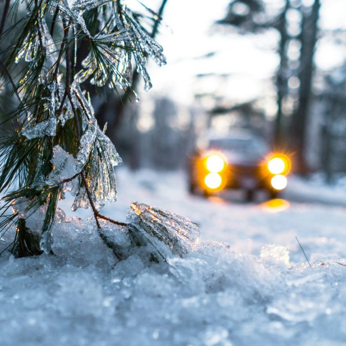 Na snímke sa auto pohybuje po zasneženej ceste, v popredí je detail na zasneženú vetvičku ihličnatého stromu.