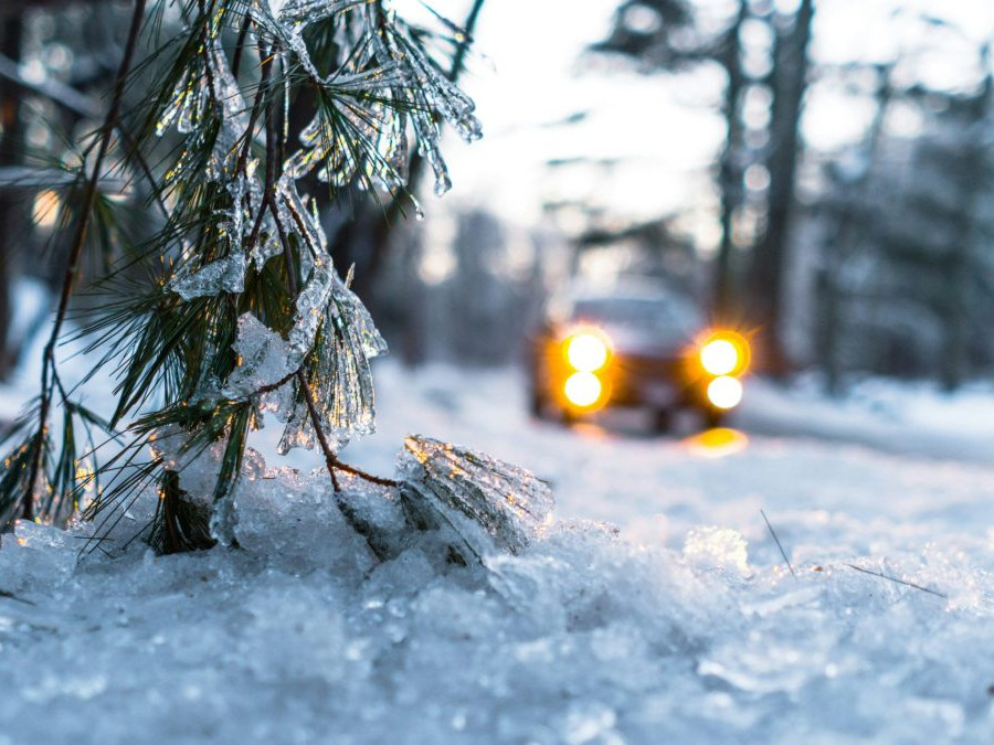 Na snímke sa auto pohybuje po zasneženej ceste, v popredí je detail na zasneženú vetvičku ihličnatého stromu.
