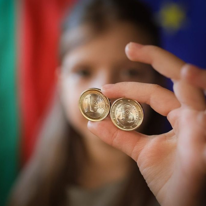 Dievča ukazuje nové euromince s bulharskými symbolmi v Sofii.