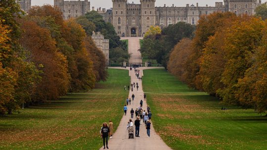 Na snímke sú ľudia na chodníku v parku, v pozadí hrad Windsor.