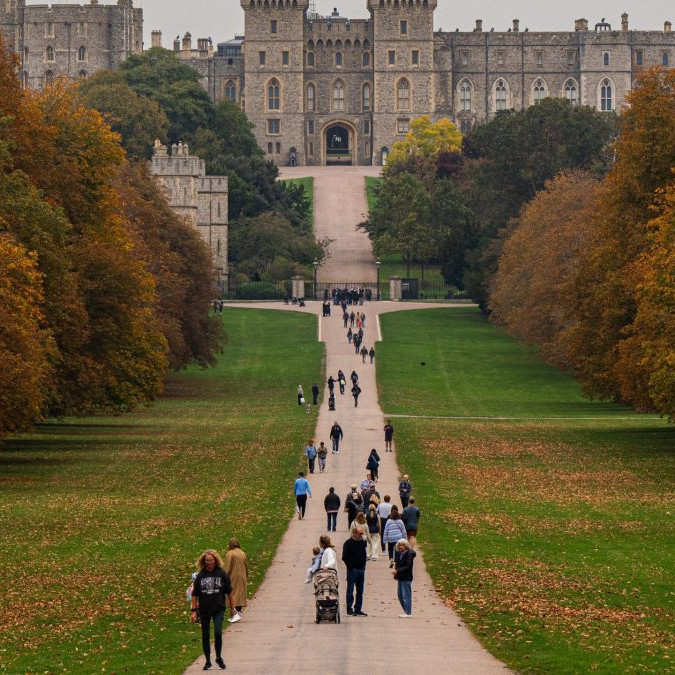 Na snímke sú ľudia na chodníku v parku, v pozadí hrad Windsor.
