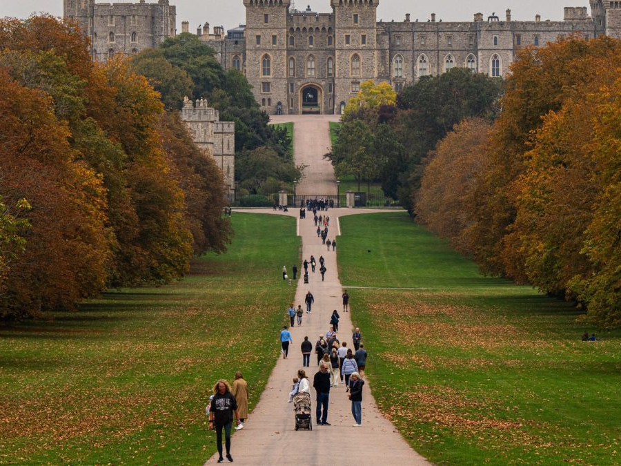 Na snímke sú ľudia na chodníku v parku, v pozadí hrad Windsor.
