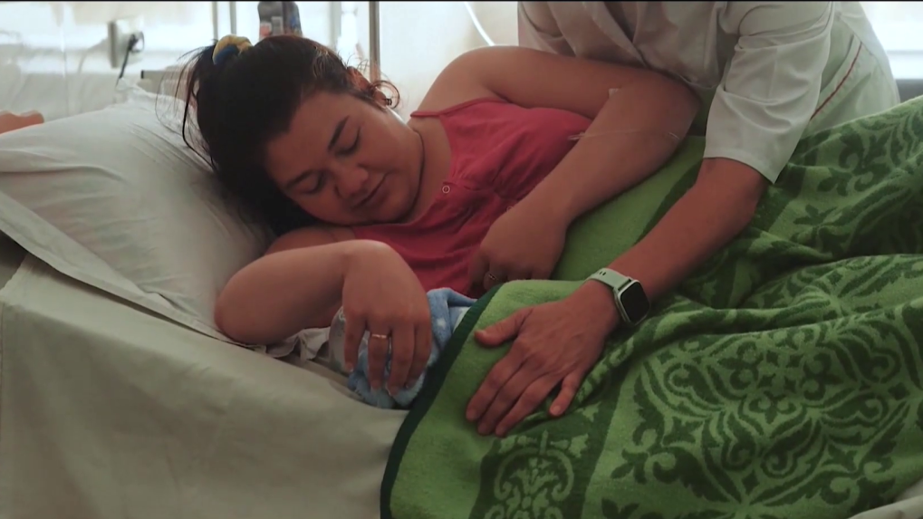 Na snímke je matka v pôrodnici s novorodencom. Z ňou stojí pôrodná sestra.