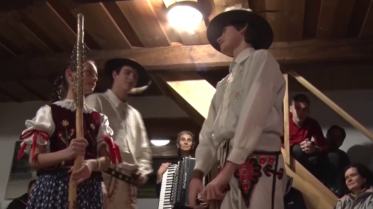 Na snímke sú mladí ľudia v krojoch v interiéri drevenice.