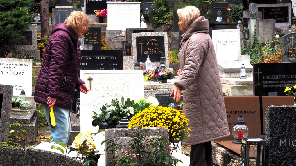 Ženy upratujú z hrobu napadané lístie na cintoríne.
