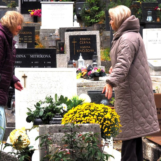 Ženy upratujú z hrobu napadané lístie na cintoríne.