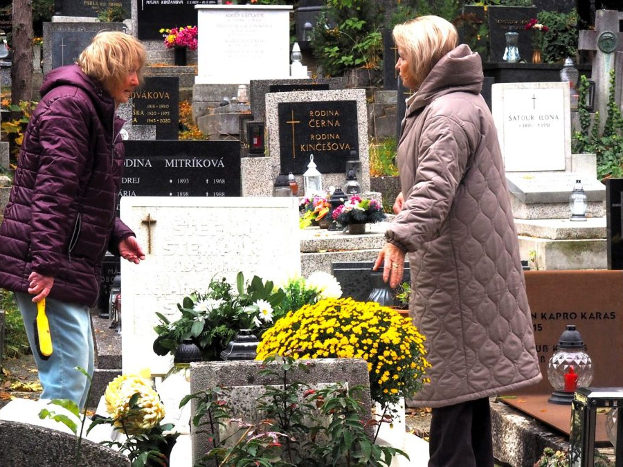 Ženy upratujú z hrobu napadané lístie na cintoríne.
