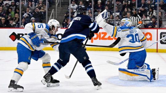 Brankár St. Louis Blues Joel Hofer (30) zasahuje, zatiaľ čo Tyler Tucker (75) bráni proti Vladislavovi Namestnikovovi z Winnipeg Jets.