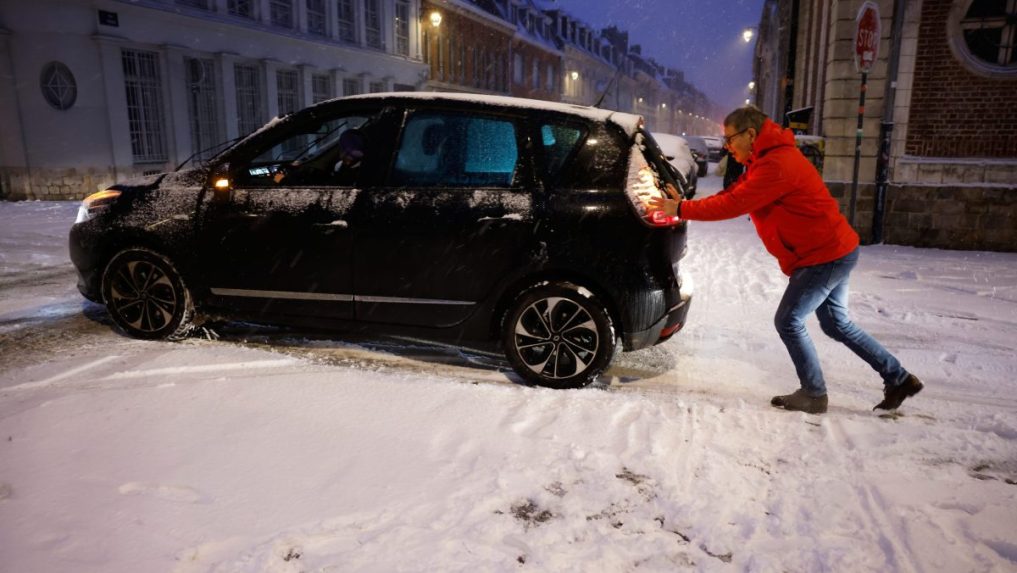Muž tlačí svoje auto počas sneženia v Lille v severnom Francúzsku.