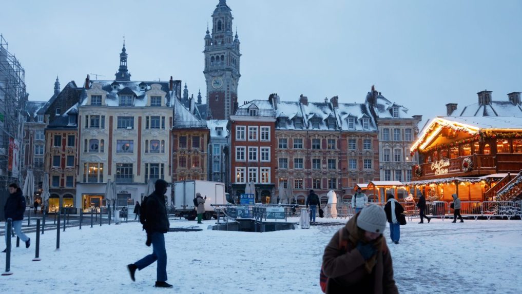 Ľudia kráčajú zasneženým námestím v Lille.