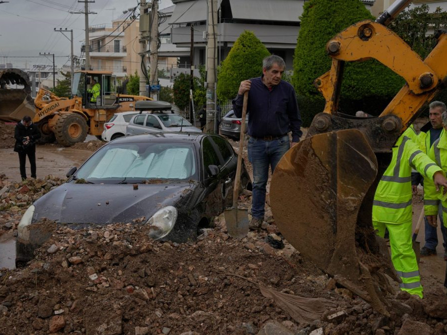 Pracovníci mestských služieb a obyvatelia odstraňujú blato a trosky z ulice vedľa poškodeného auta po povodniach spôsobených silnými dažďami.