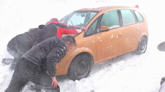 Na snímke muži pomáhajú tlačiť auto zapadnuté v záveji.