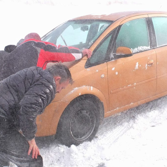 Na snímke muži pomáhajú tlačiť auto zapadnuté v záveji.