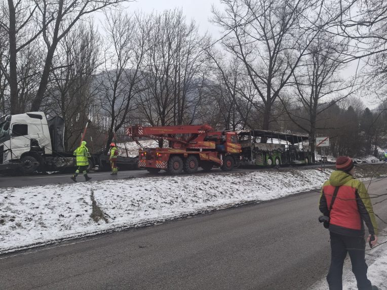 Na snímke v pozadí zhorený autobus po nehode.