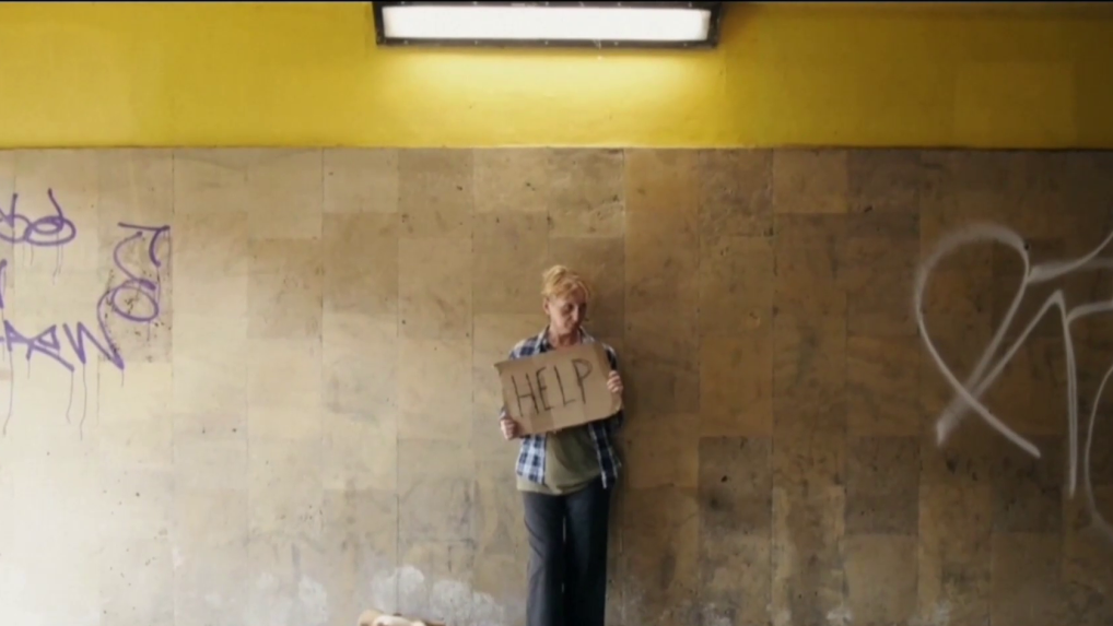 Na snímke žena bez domova stojí v podchode držiac nápis "Pomoc" napísaný na kartóne.