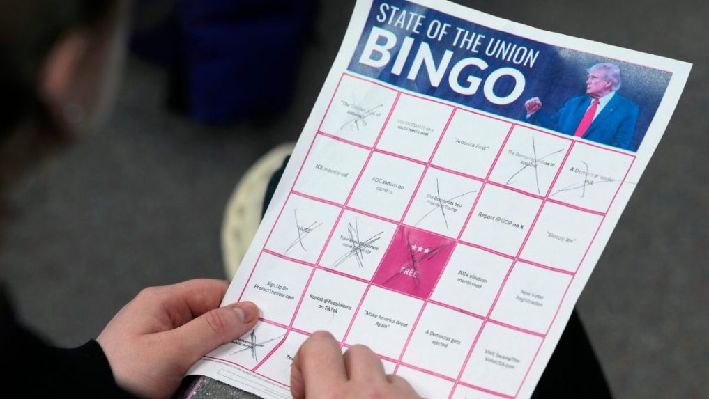 Žena vypĺňa bingo kartu, zatiaľ čo sleduje prezidenta Donalda Trumpa,