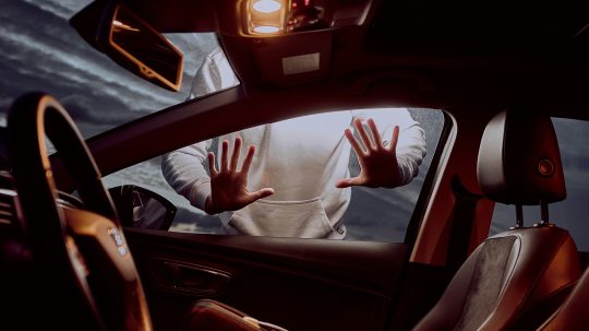 Na snímke je interiér auta, za oknom pasažiera je postava muža, dotýka sa okna oboma rukami.