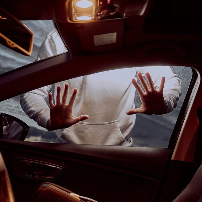 Na snímke je interiér auta, za oknom pasažiera je postava muža, dotýka sa okna oboma rukami.