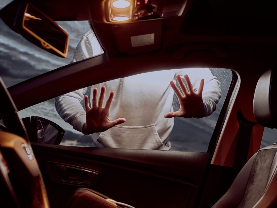 Na snímke je interiér auta, za oknom pasažiera je postava muža, dotýka sa okna oboma rukami.