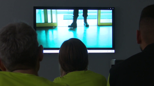 Osoby sledujú plátno, na ktorom sa premieta video.