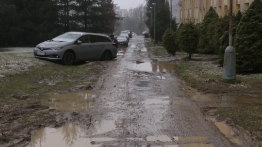 Na snímke je zablatená cesta, na trávniku vyjazdené jamy a jarky,