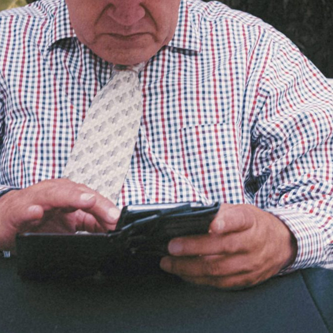 Na snímke senior v košeli s kravatou pracuje so smartfónom.