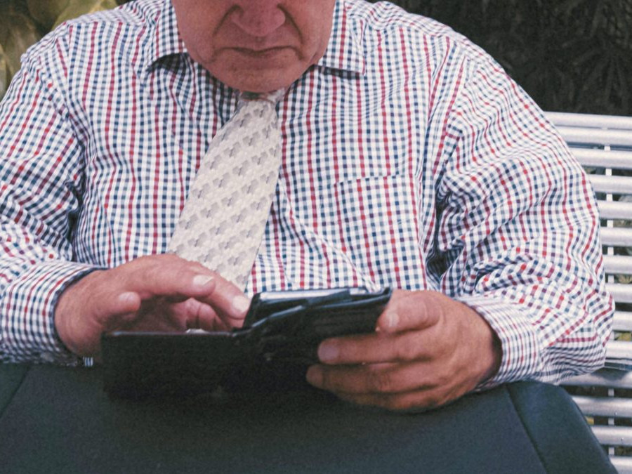 Na snímke senior v košeli s kravatou pracuje so smartfónom.