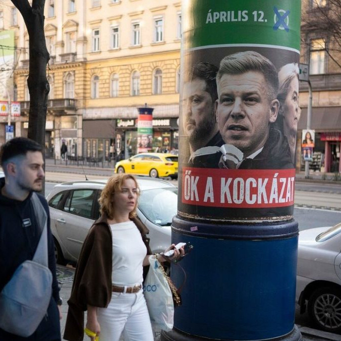 Ľudia prechádzajú okolo plagátu, ktorý propaguje stranu Fidesz.