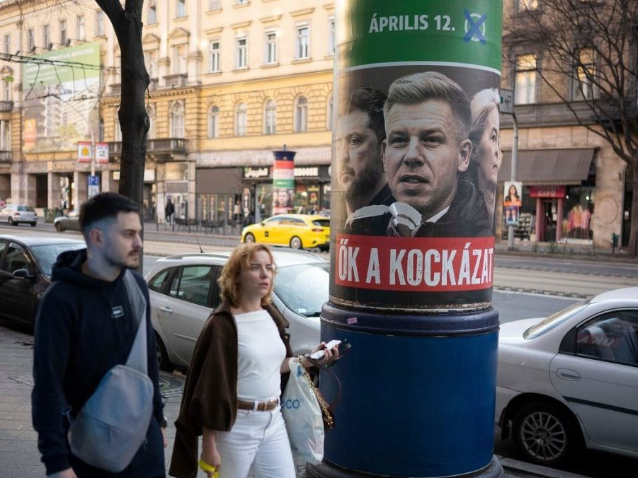 Ľudia prechádzajú okolo plagátu, ktorý propaguje stranu Fidesz.