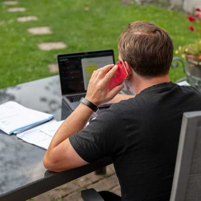 Muž sedí doma v záhrade a pracuje na svojom notebooku.