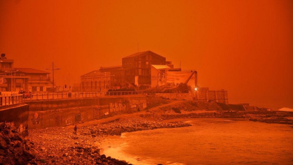 Muž kráča po pláži počas piesočnej búrky na Kréte.