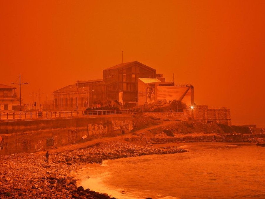 Muž kráča po pláži počas piesočnej búrky na Kréte.