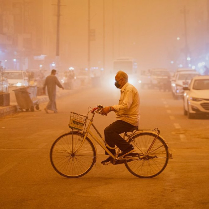 Muž s maskou na bicykli počas prachovej búrky v Nadžafe.