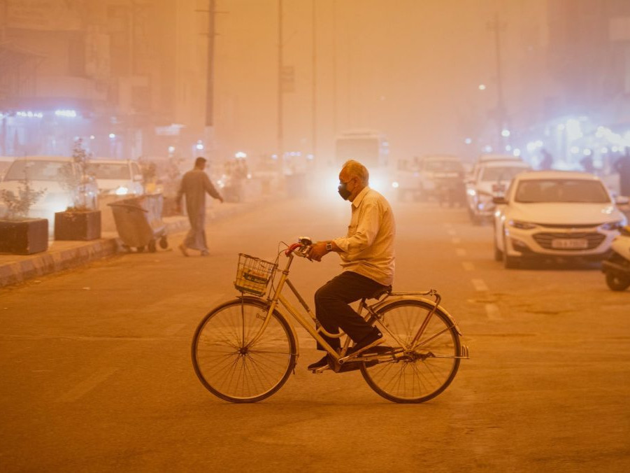 Muž s maskou na bicykli počas prachovej búrky v Nadžafe.