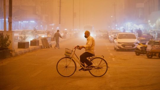Muž s maskou na bicykli počas prachovej búrky v Nadžafe.
