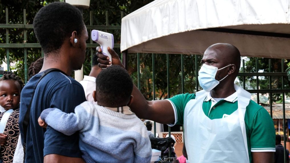 Pracovník nemocnice meria teplotu osobám pred vstupom do budovy v ugandskom meste Kampala.