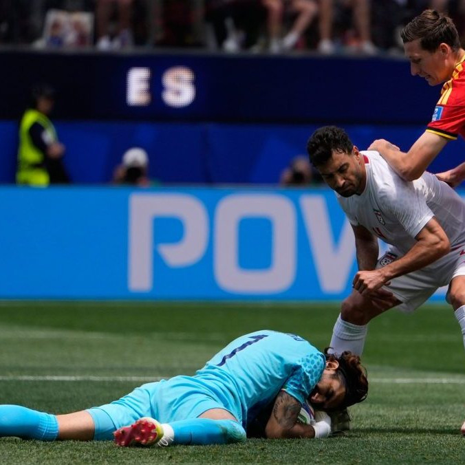 Iránsky brankár Alireza Beiranvand na zemi s chytenou loptou.