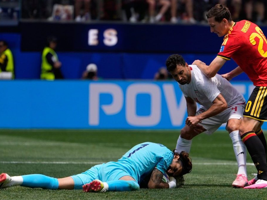 Iránsky brankár Alireza Beiranvand na zemi s chytenou loptou.