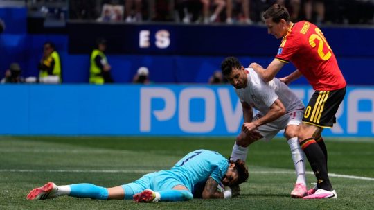 Iránsky brankár Alireza Beiranvand na zemi s chytenou loptou.