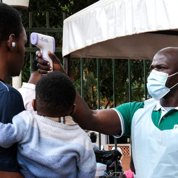 Pracovník nemocnice meria teplotu osobám pred vstupom do budovy v ugandskom meste Kampala.