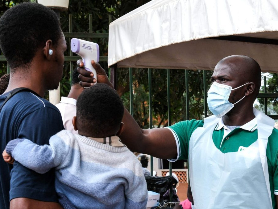 Pracovník nemocnice meria teplotu osobám pred vstupom do budovy v ugandskom meste Kampala.