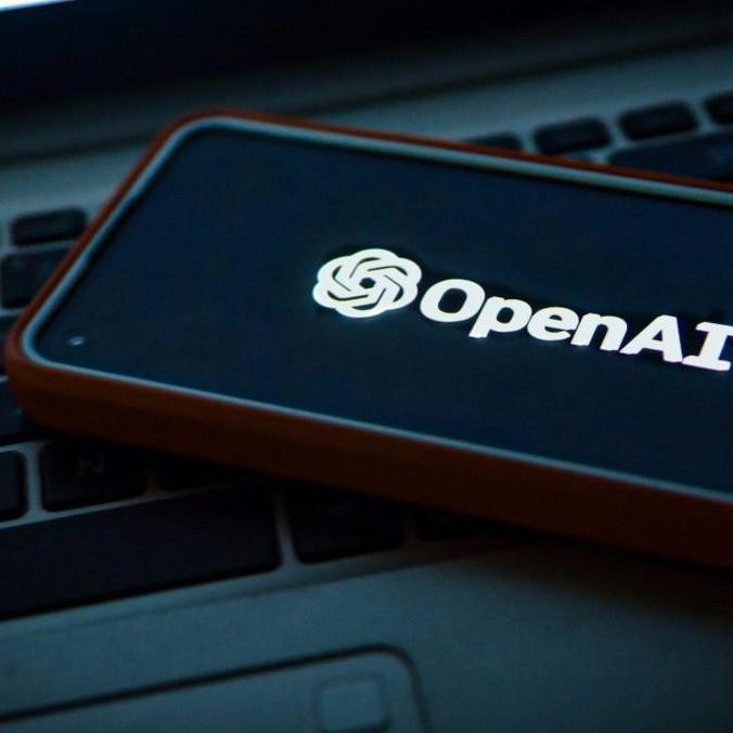 Na snímke telefón s logom OpenAI položený na notebooku.