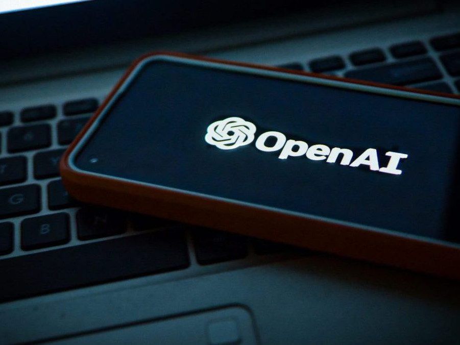 Na snímke telefón s logom OpenAI položený na notebooku.