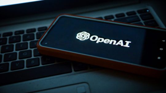 Na snímke telefón s logom OpenAI položený na notebooku.