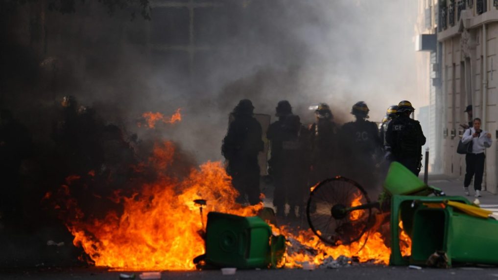 Policajti stoja pred horiacimi ko&scaron;mi a čelia &scaron;tudentom počas protestu.