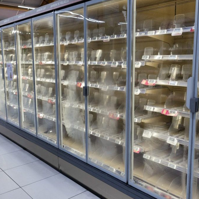 Žena prechádza okolo prázdnych chladničiek v supermarkete.